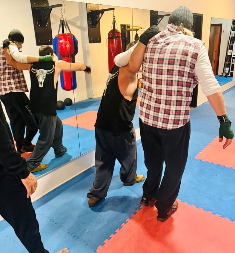 A coach supporting an adaptive boxer during a training session in the gym