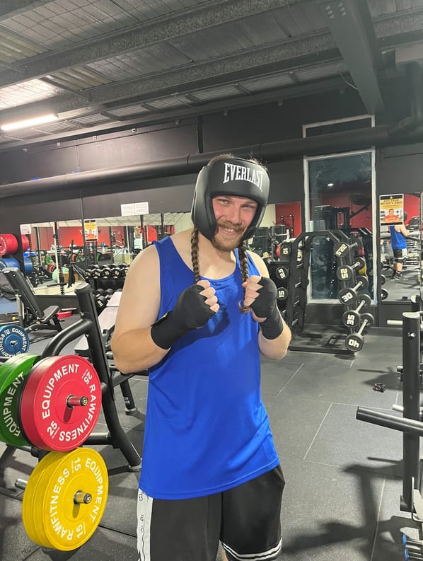 An adaptive boxer wearing headgear and hand wraps smiling in a gym