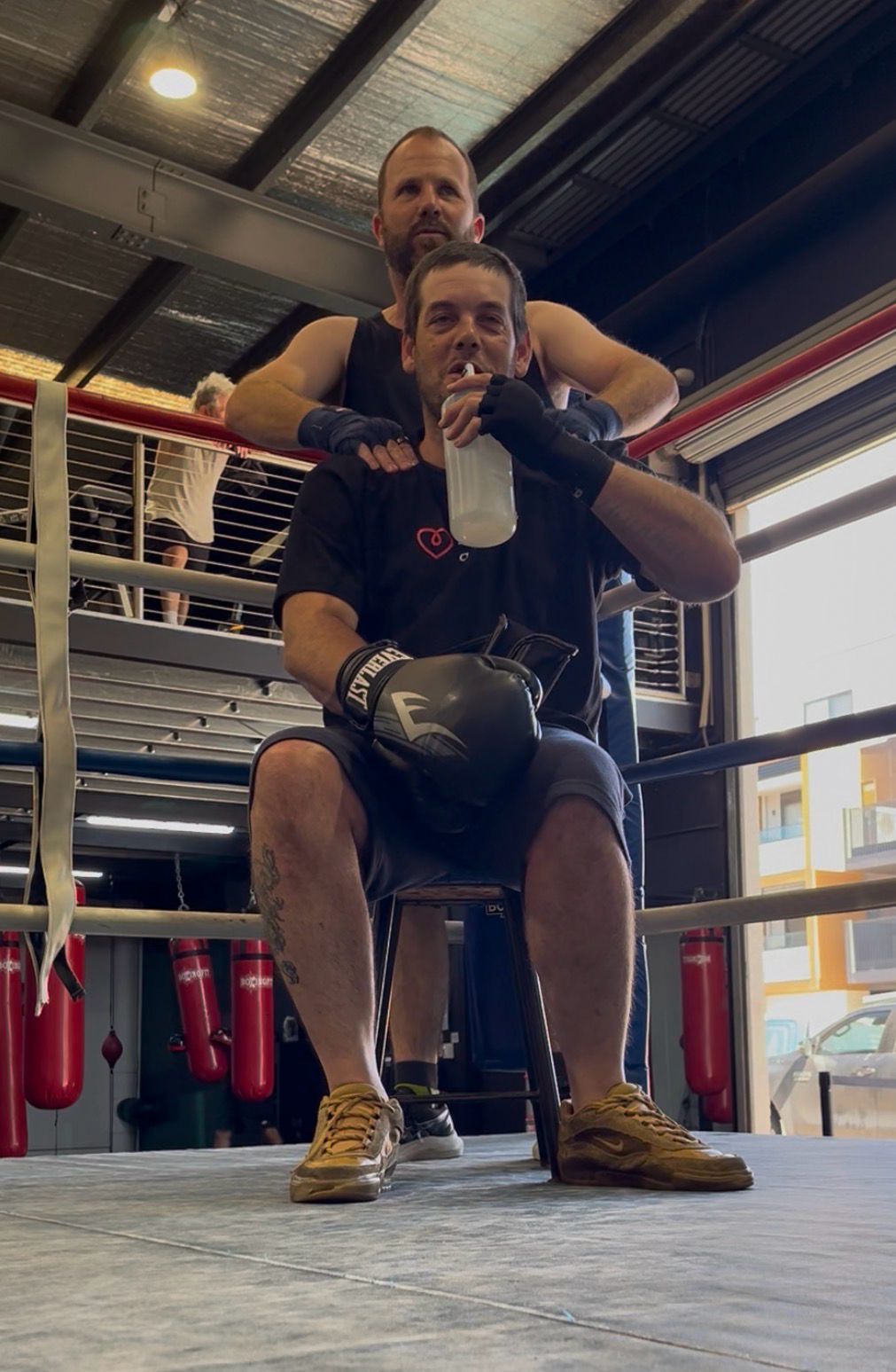 A boxer takes water in the corner between rounds while his coach steadies him from behind