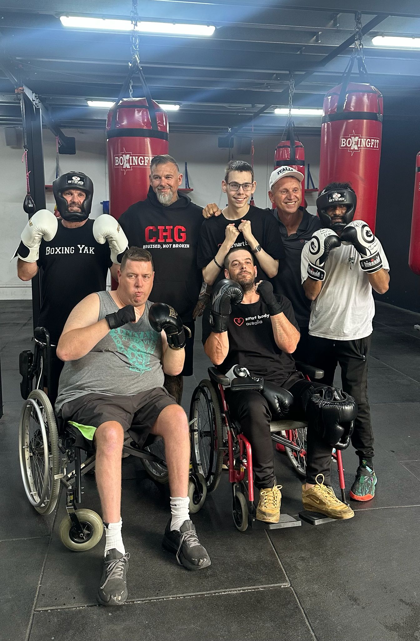 A group of adaptive boxers and their coaches pose together with gloves raised in the gym